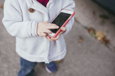 Low section of girl holding smart phone while standing on footpath