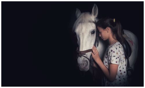 Girl touching horse while standing against black background