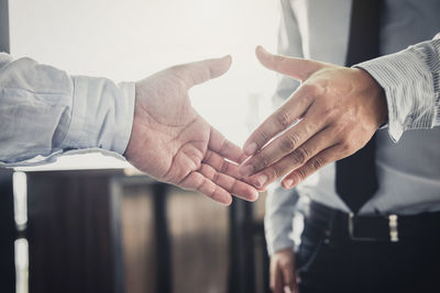 Midsection of colleagues hands reaching for handshake in office