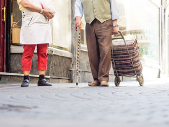 Low section of senior couple with wheeled luggage on footpath in city