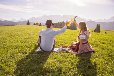 Rear view of couple toasting beer glasses on grassy field