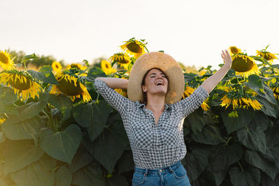 Beautiful young woman with sunflowers enjoying nature and laughing on summer sunflower field.