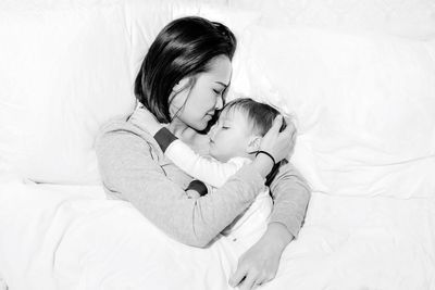 Directly above shot of mother embracing son while sleeping on bed at home