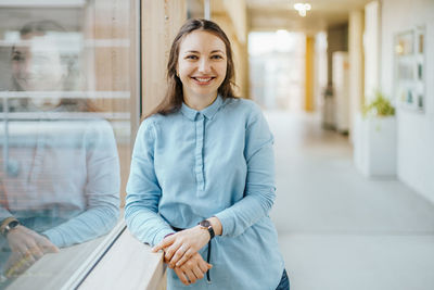 Portrait of happy young businesswoman standing at office corridor