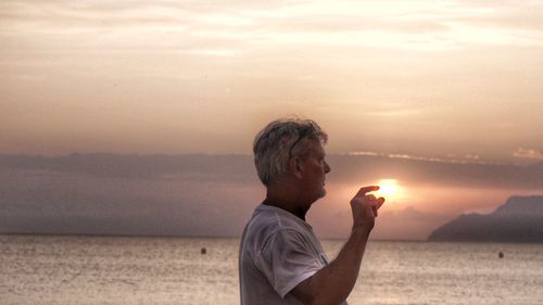 Side view of man at beach against sky during sunset