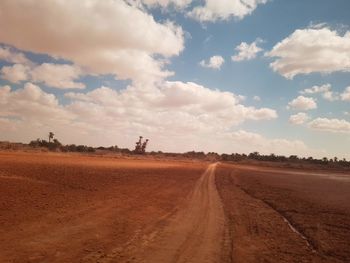 Dirt road amidst field against sky