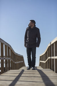 Full length of mature man walking on footbridge against clear blue sky