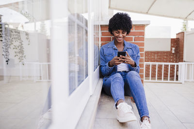 Happy woman using smart phone sitting on porch