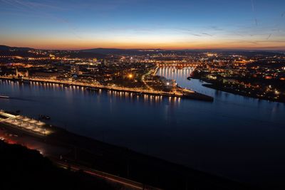 High angle view of illuminated buildings by river against sky at sunset