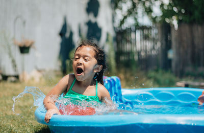 Mixed race young girl at home having fun on hot summer day in kiddie pool