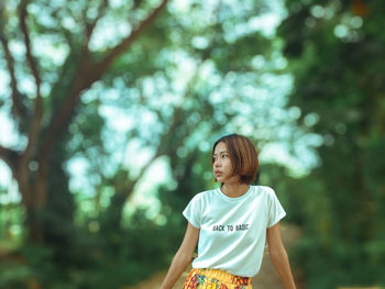 Woman looking away while standing against trees