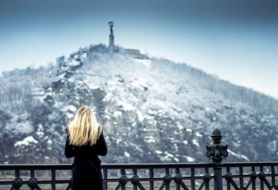 Rear view of woman standing on railing against mountain