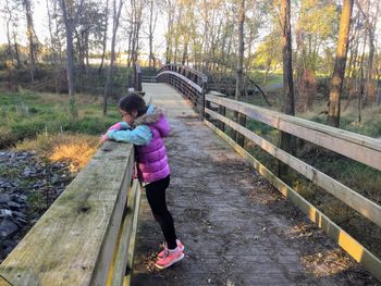 Girl standing by railing on footbridge at park