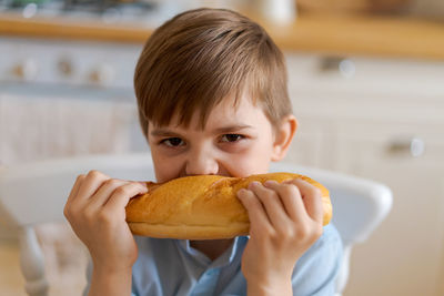 Happy handsome young teenage boy holding and eating freshly baked bread.