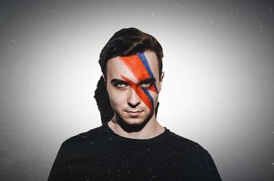 Portrait of young man with face paint against gray background