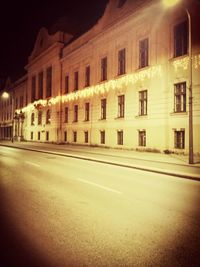 Illuminated road by building at night