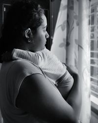 Side view of woman looking through window at home