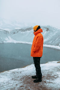 Side view of young tourist on peak of mountain in snow looking at water in valley