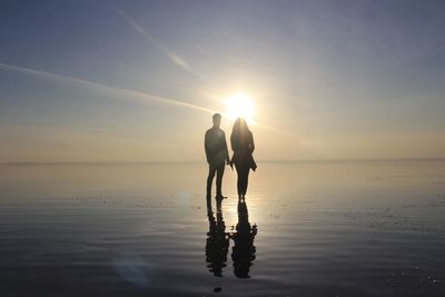 People at beach against sky during sunset