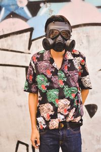 Portrait of man wearing gas mask while standing graffiti wall