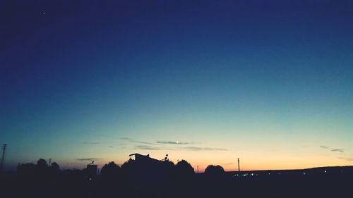 Silhouette trees against clear blue sky during sunset