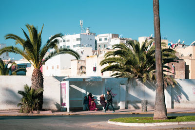 People by palm trees in city against sky