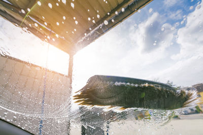 Close-up of wet glass window against sky