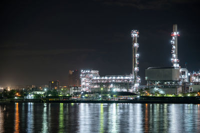 Illuminated city by river against sky at night