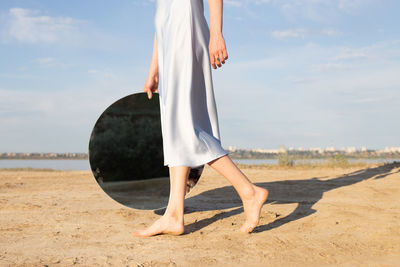 Low section of woman holding mirror walking on field