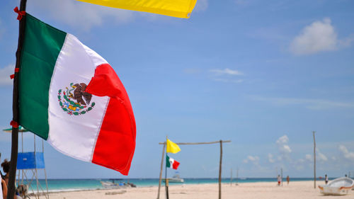 Mexican flag on beach against sky