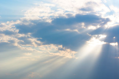 Low angle view of sunlight streaming through clouds