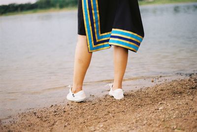 Low section of woman standing at lakeshore