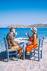 People sitting on chair at beach against clear sky