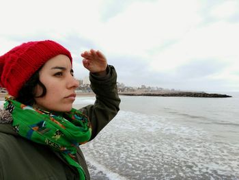 Portrait of young woman standing at beach against sky