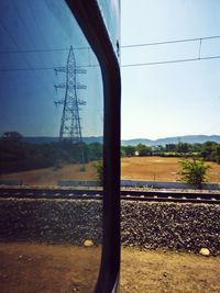 Electricity pylon by landscape against sky seen through window