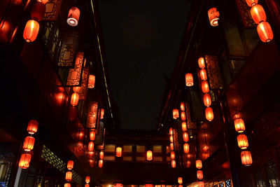 Low angle view of illuminated lanterns hanging amidst buildings at night