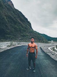 Full length of shirtless man standing on mountain against sky