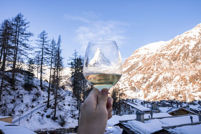 Man holding wineglass viewing matterhorn and snow covered townscape against sky