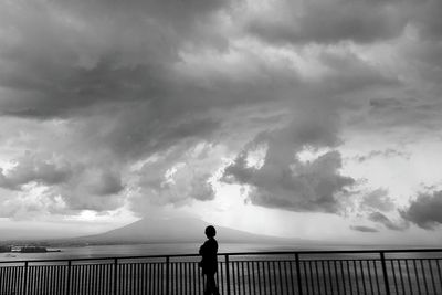 Rear view of people standing on bridge against cloudy sky