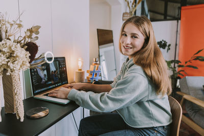 Portrait of smiling young woman using phone while sitting on table