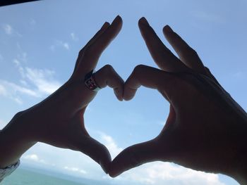 Low angle view of hand holding heart shape against sky