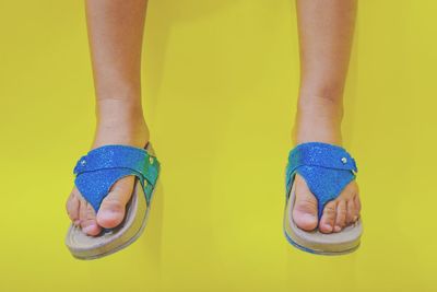 Low section of child standing against yellow background