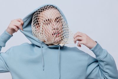 Man pulling mesh bag wearing it on face against gray background