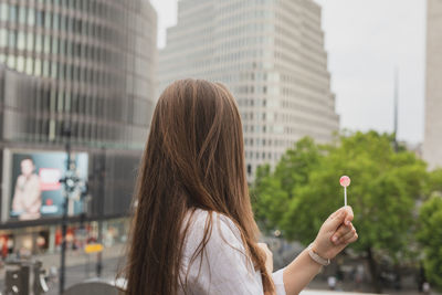 Side view of woman holding lollipop against buildings in city