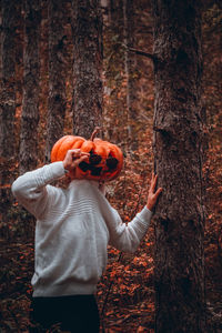 Woman standing by tree trunk in forest during autumn