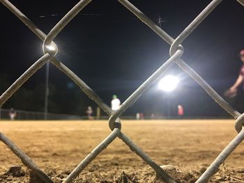 Close-up of illuminated chainlink fence against sky at night