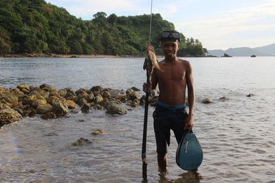 Portrait of young man fishing in river against sky