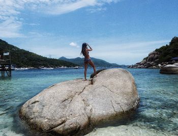 Woman standing on rock at beach against sky