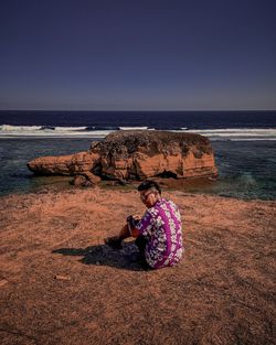 Man sitting on rock at beach against sky