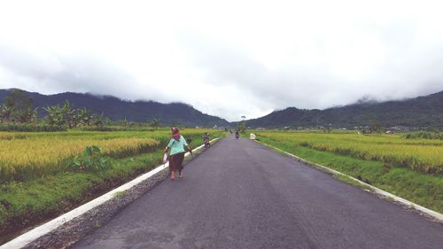 Rear view of woman walking on road by agricultural field against sky